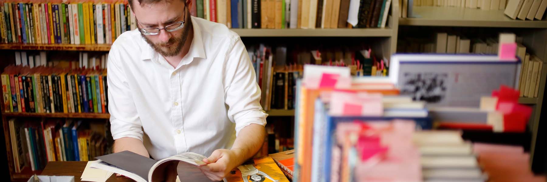 Surrounded by a boxes of books, a man thumbs through an old comic book.