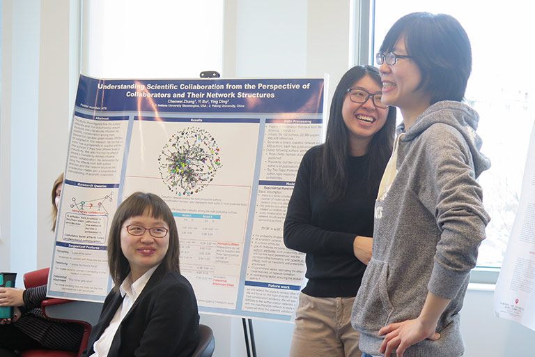 Three students stand in front of an easel showing off their research.