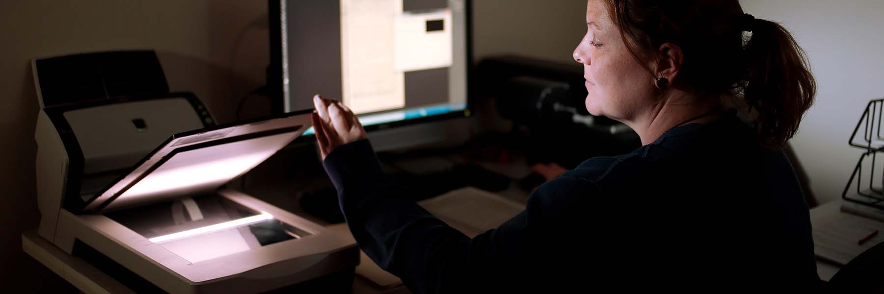 A student sits in a dark room scanning copies of historical documents.